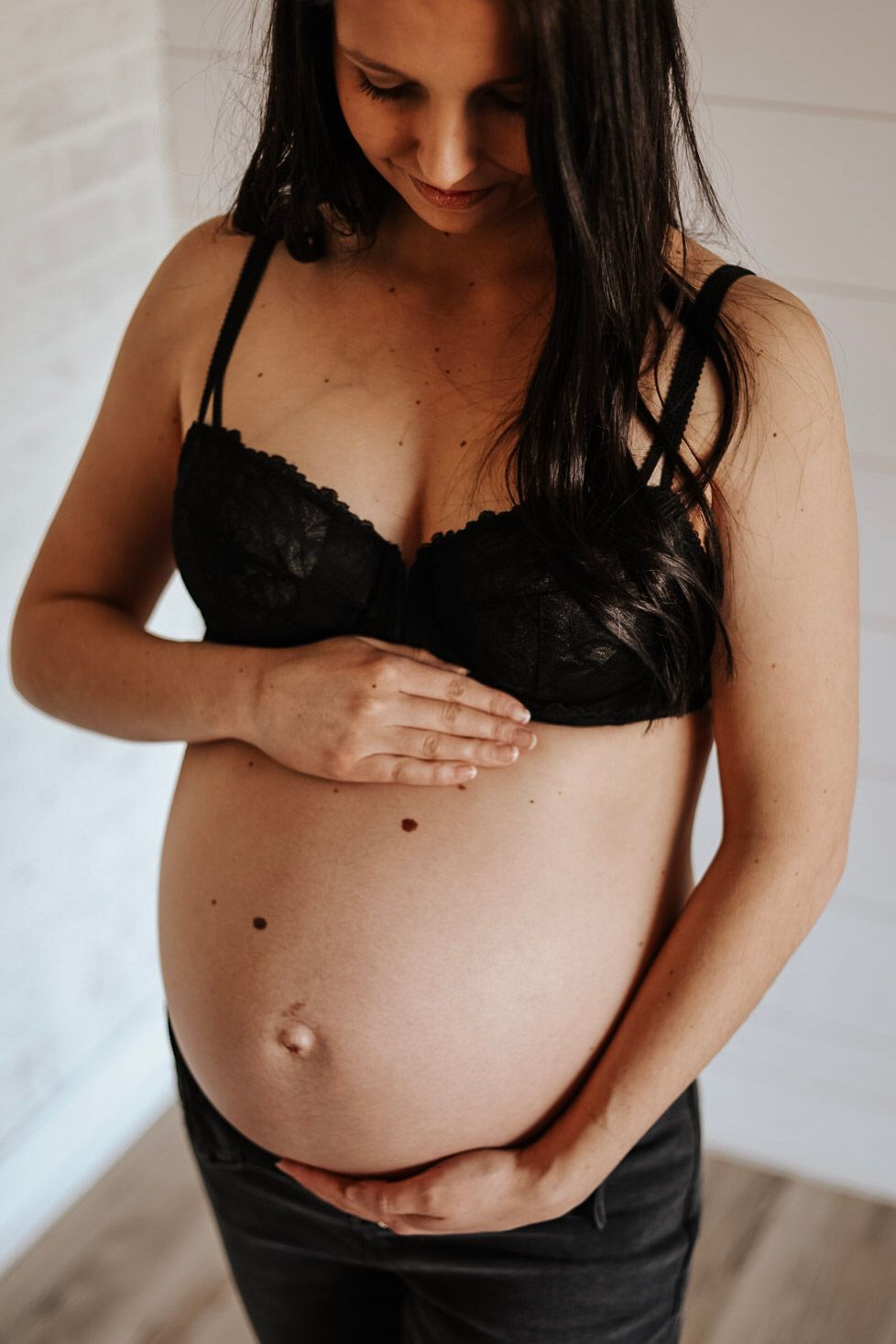 Intimate maternity photo showing an expectant mother's belly in black lingerie against white backdrop.