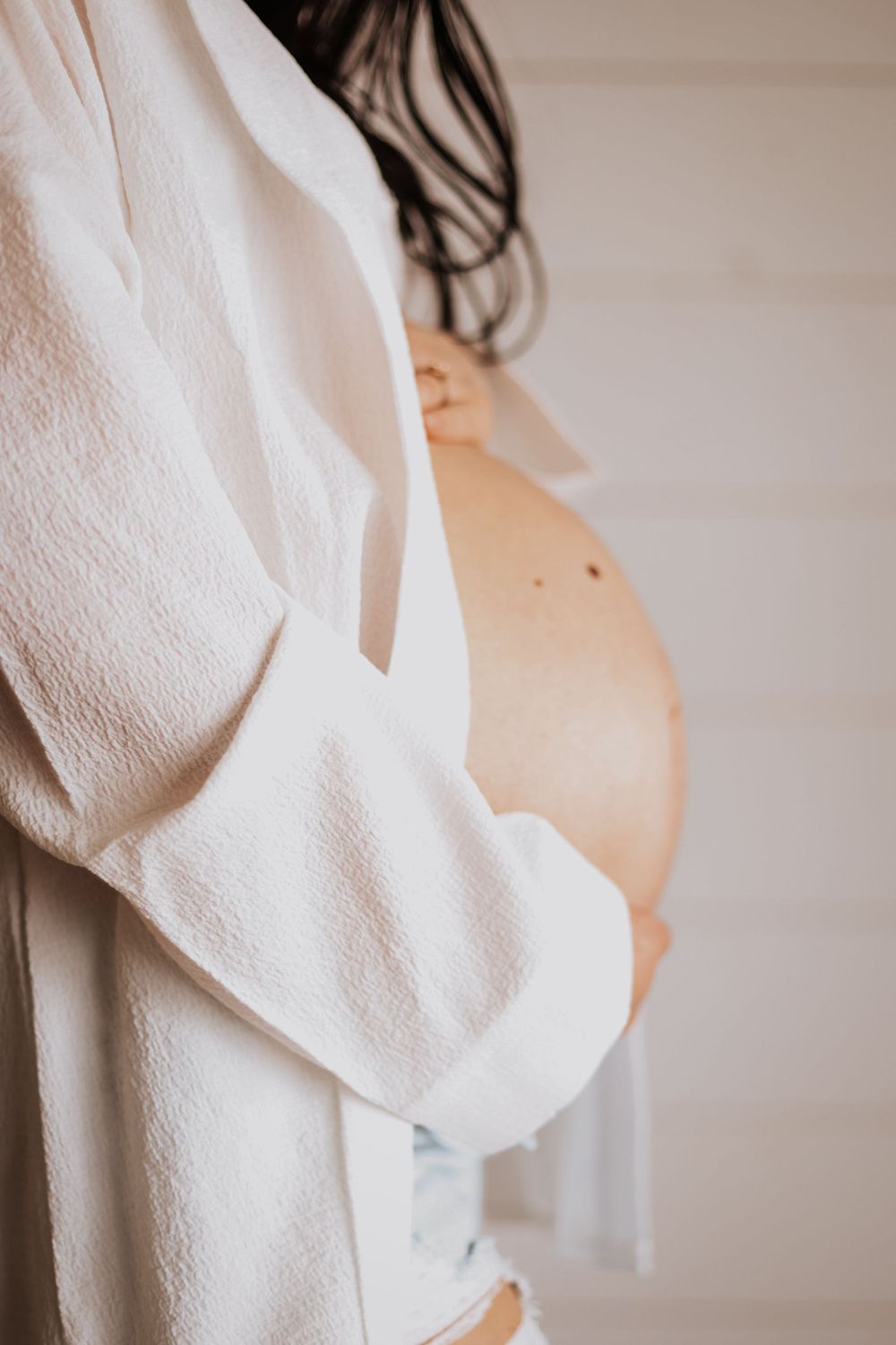 Close up of pregnant belly with white flowing shirt against shiplap wall.
