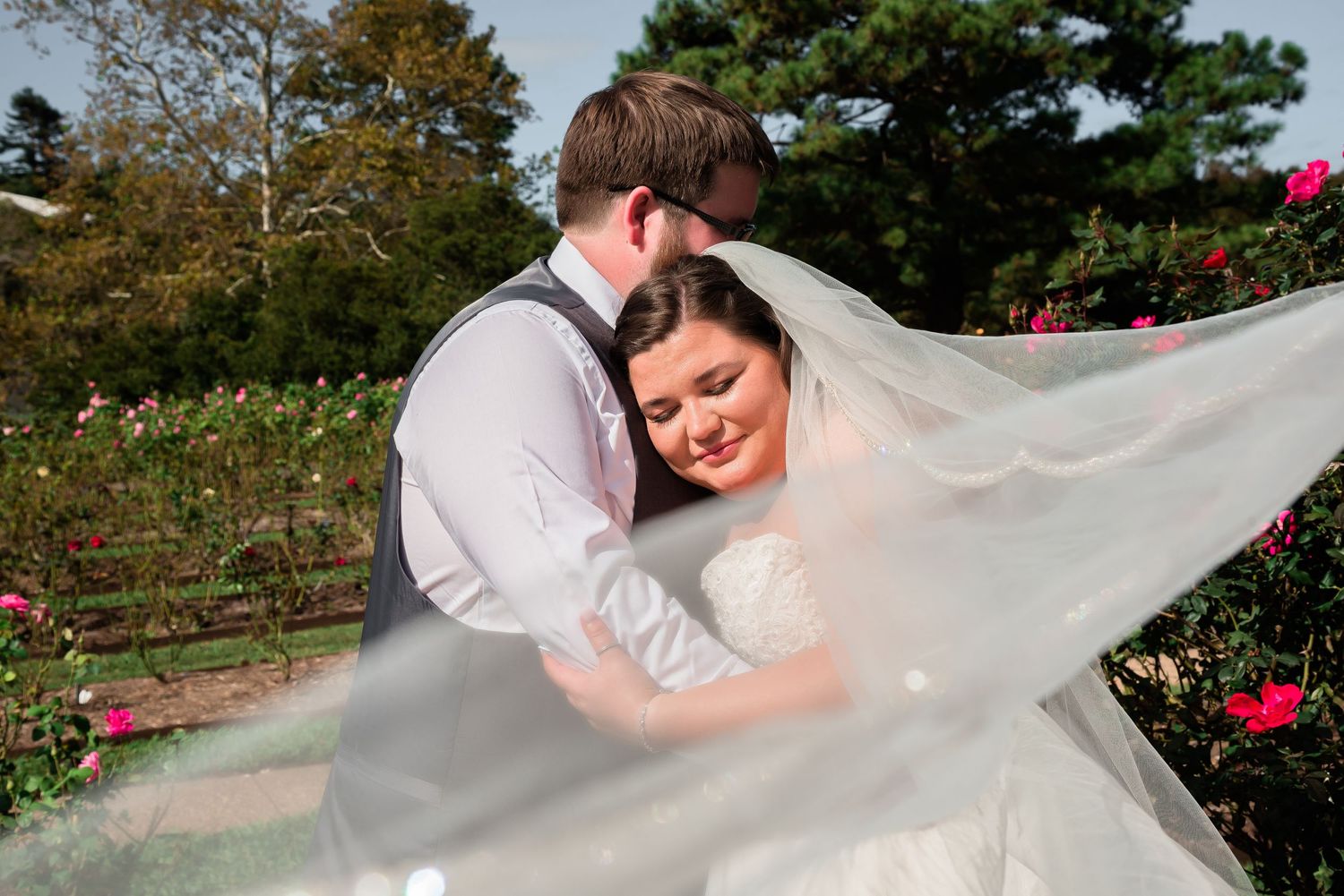 A romantic garden wedding moment with flowing veil and pink roses in the background.