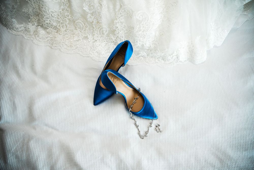 Blue high heel wedding shoes placed on white lace fabric with jewelry accents.