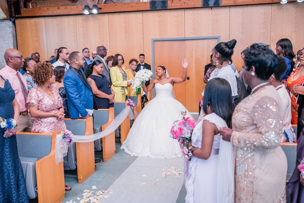Wedding guests in formal attire gather in chapel during ceremony with pink floral accents.