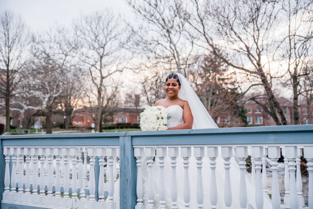 A bride in a white strapless gown poses on a light blue balcony with white railings at dusk.