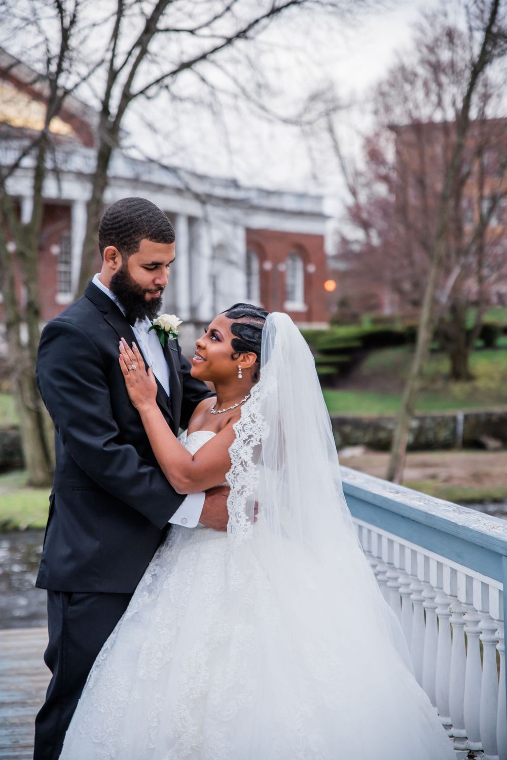 Romantic wedding couple embraces on a blue-railed balcony against a brick building backdrop.