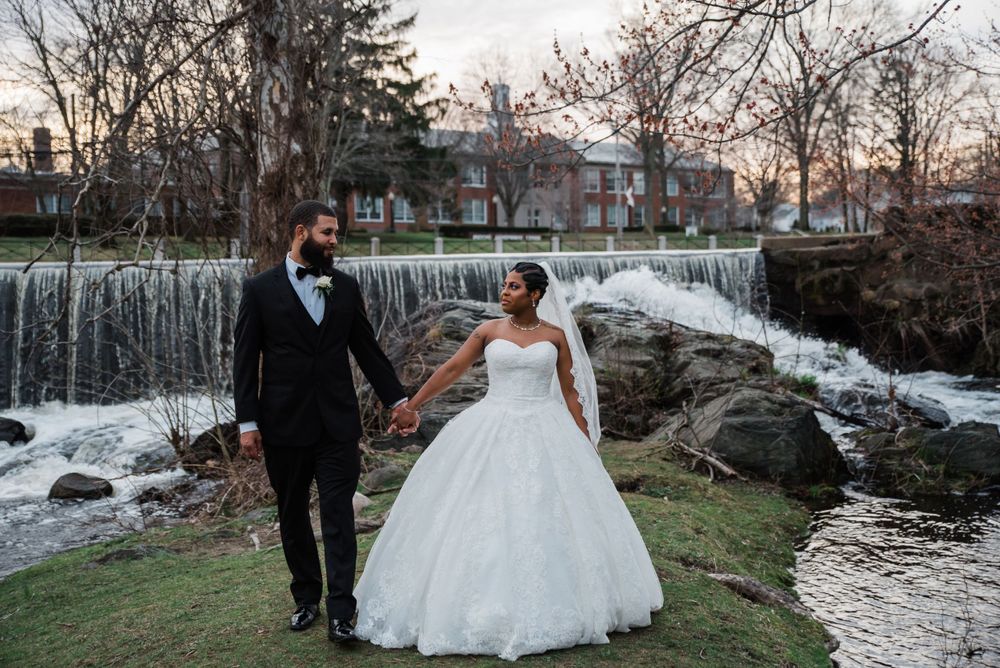 Newlyweds pose together by cascading waterfall during their outdoor wedding photoshoot.