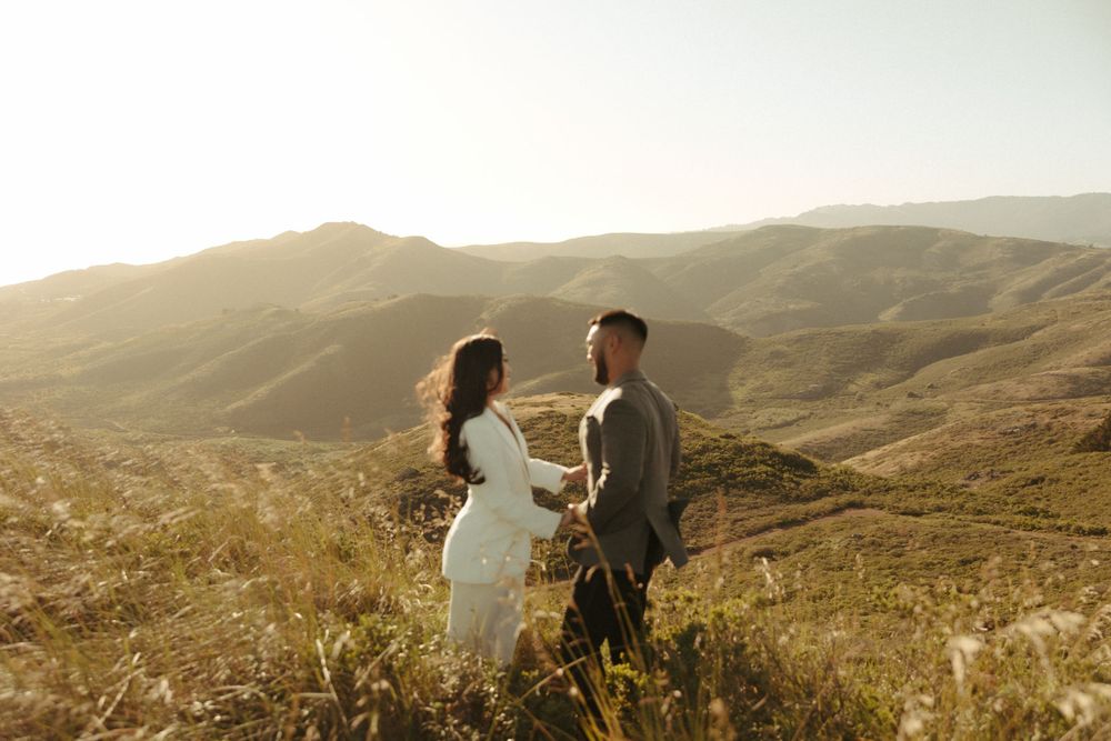 Romantic moment between two people standing in golden light on a hillside overlooking mountains.