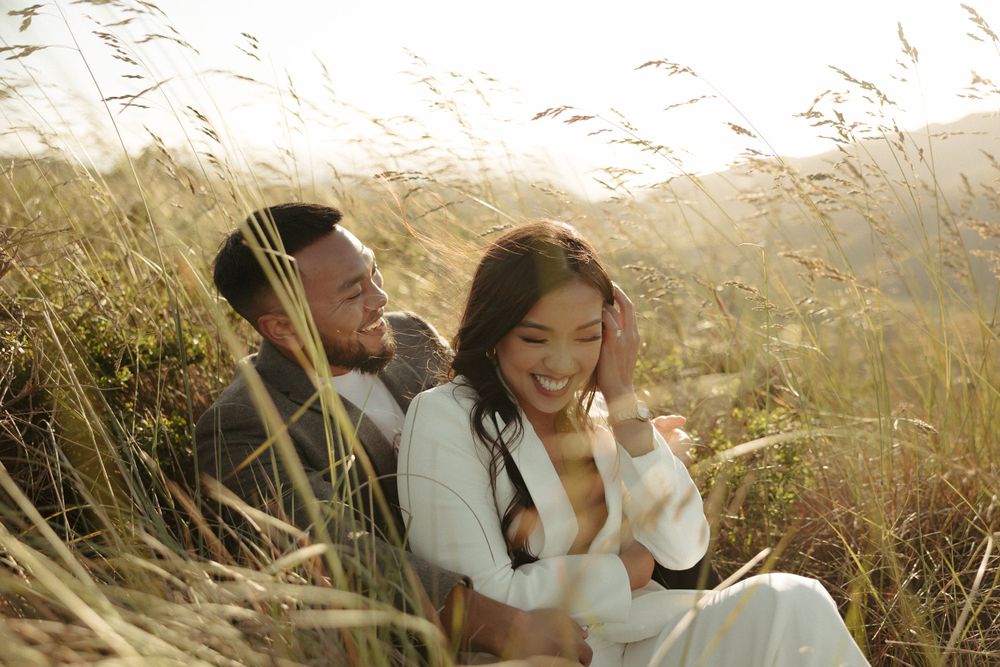 Intimate moment captured in tall golden grass during sunset with mountains in background.