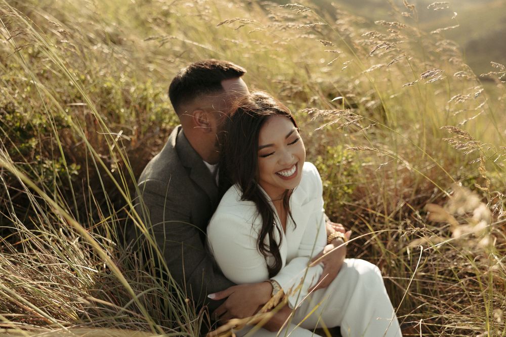 Sweet embrace photographed among tall grass with warm sunset lighting and mountain scenery.