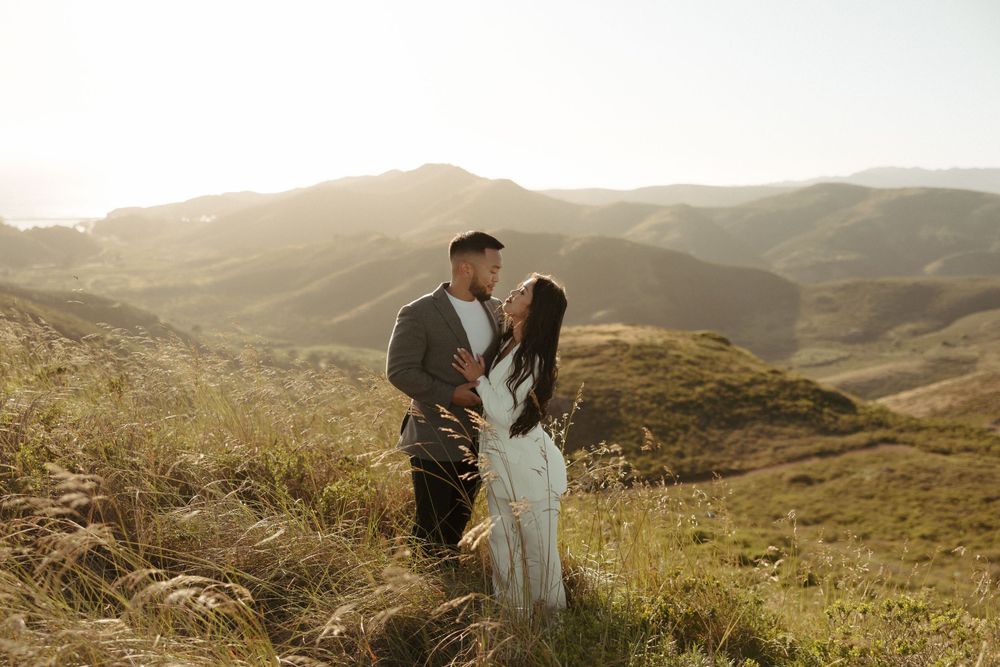 Romantic moment captured on hillside trail with rolling mountains in background during sunset.