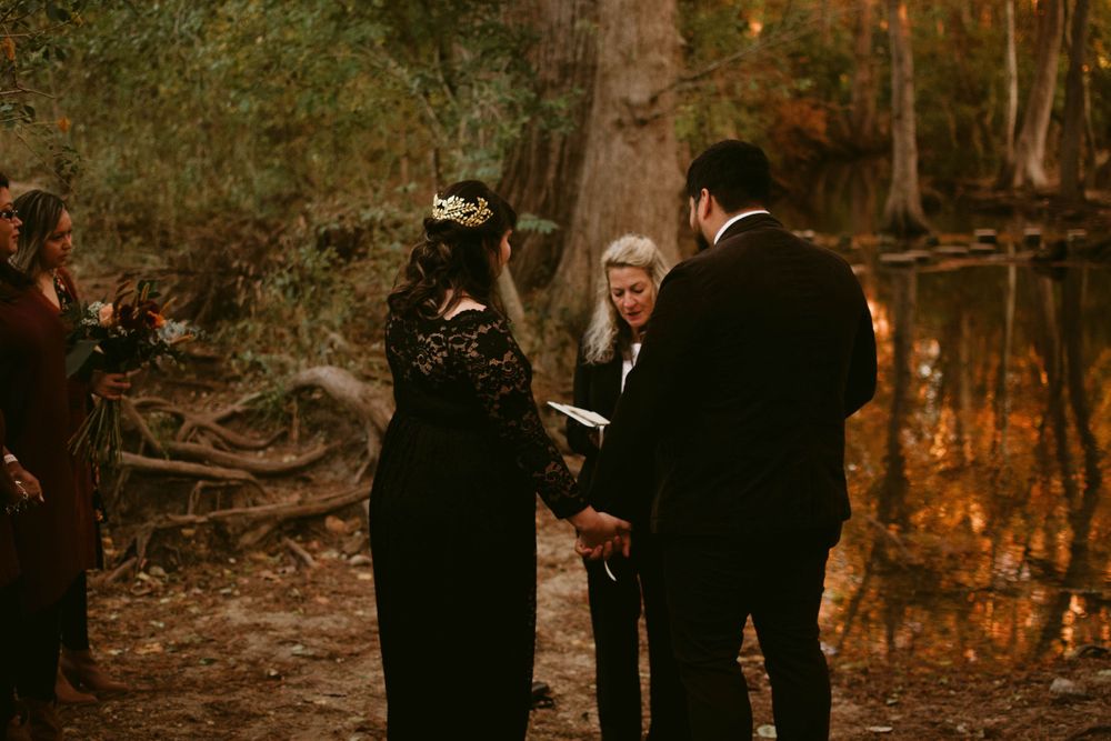 Rustic woodland wedding ceremony with couple and officiant against autumn trees.