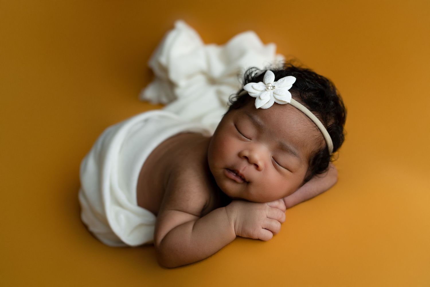 Sleeping newborn wearing white headband on orange background.