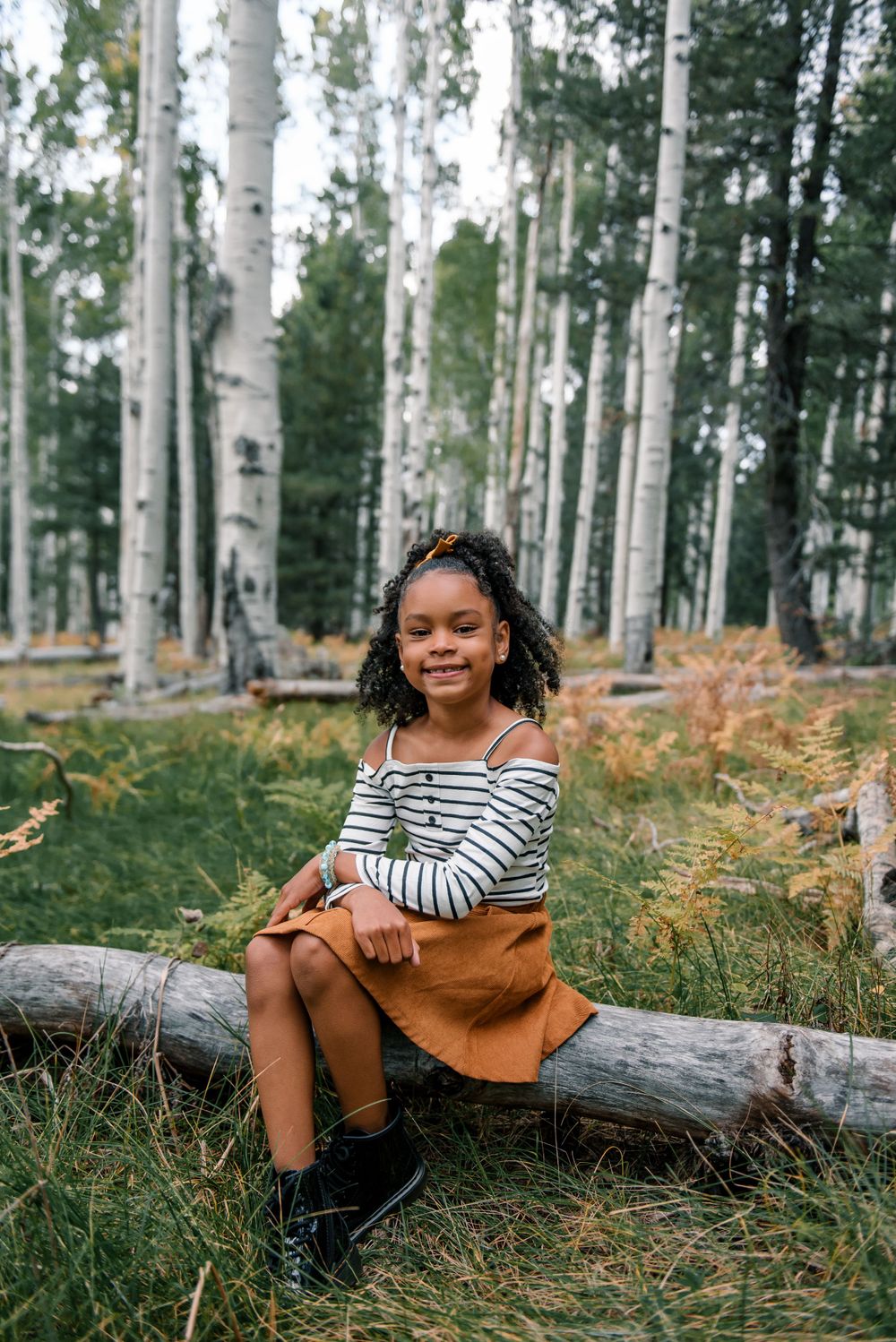 Young person in striped shirt relaxing on fallen log in autumn aspen forest.