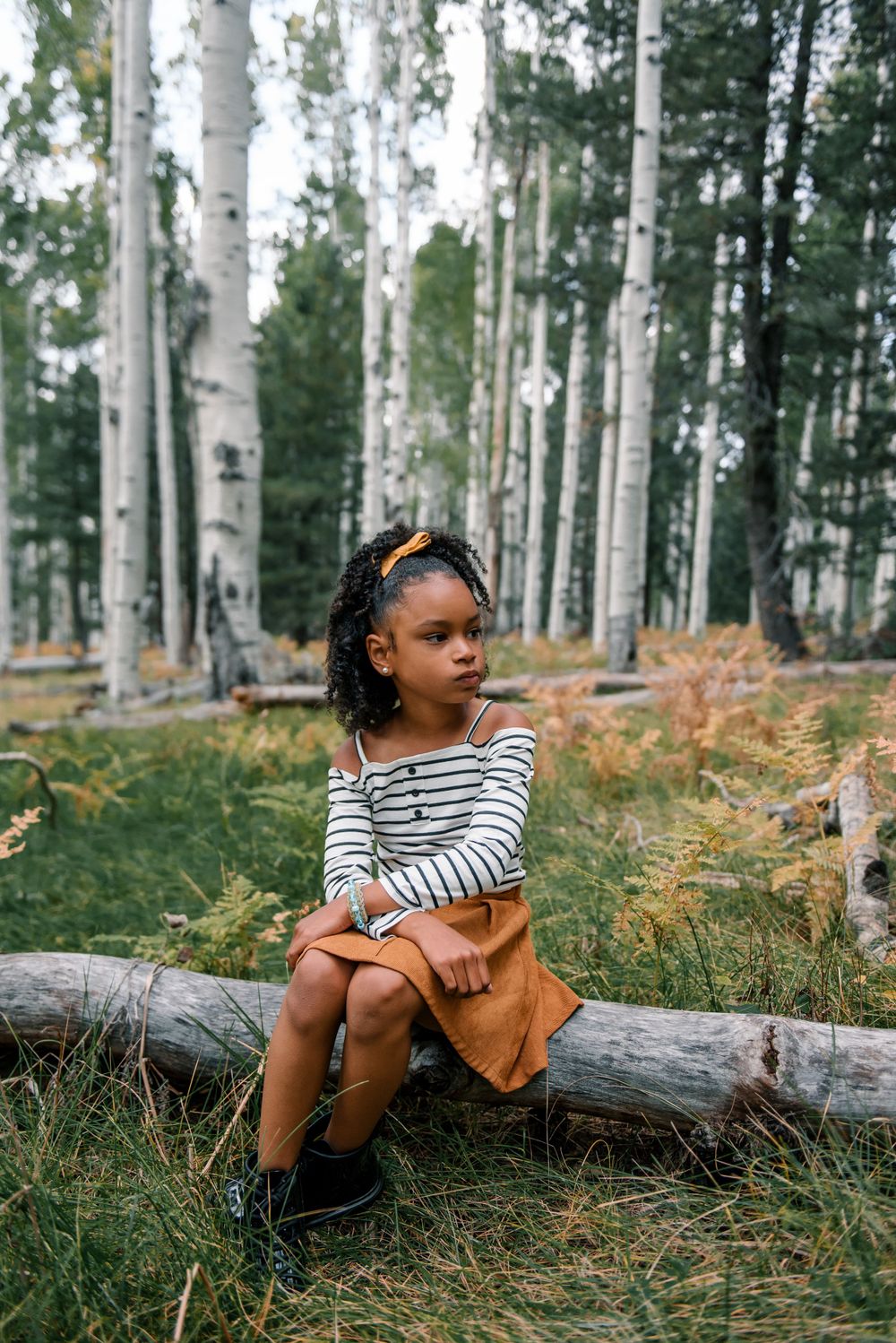 A casual outdoor photoshoot in an aspen forest with striped shirt and brown dress against autumn ferns.