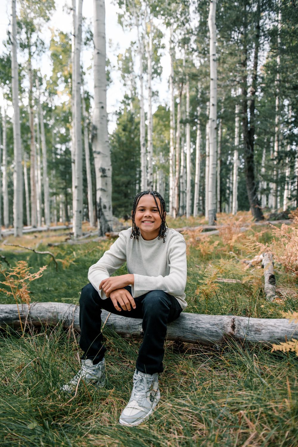 Casual portrait in aspen grove with person wearing gray sweater and sneakers on fallen log.