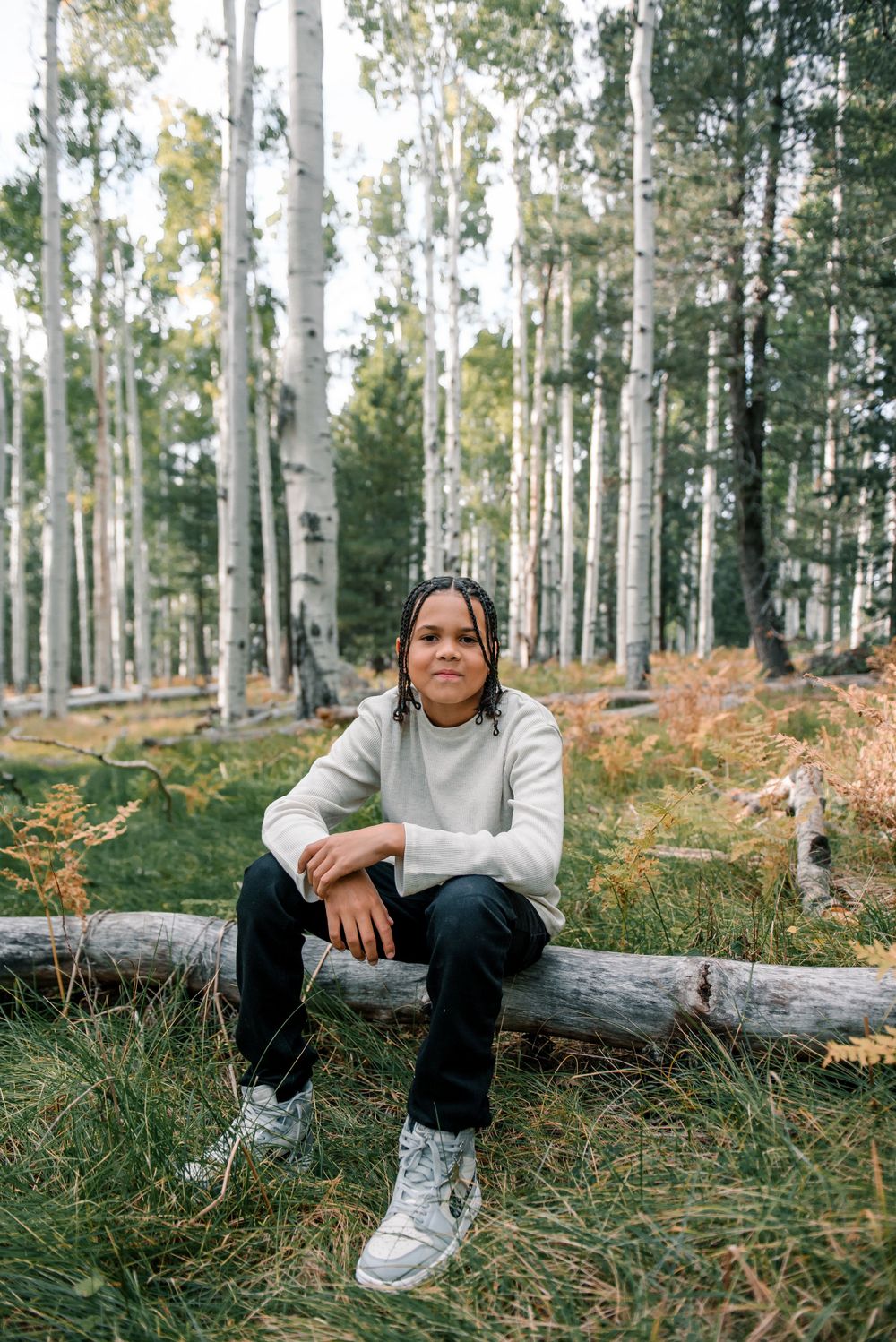 Relaxed outdoor portrait among aspen trees with person sitting on fallen log in casual attire.
