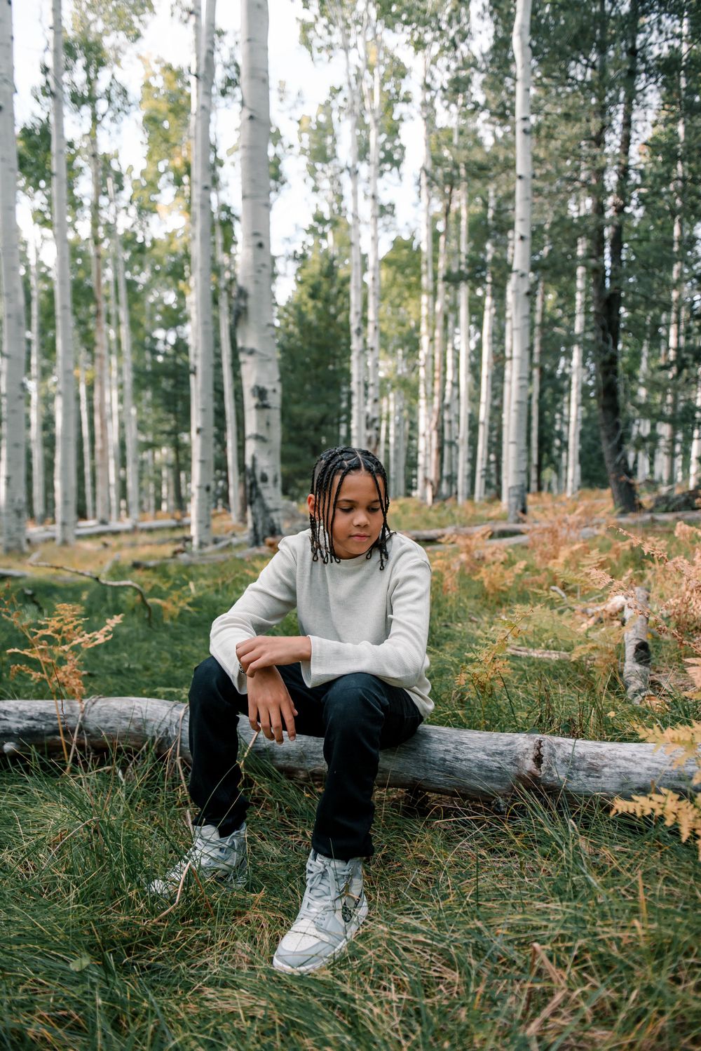 Natural forest setting with person in gray sweater and dark pants sitting on fallen tree trunk.