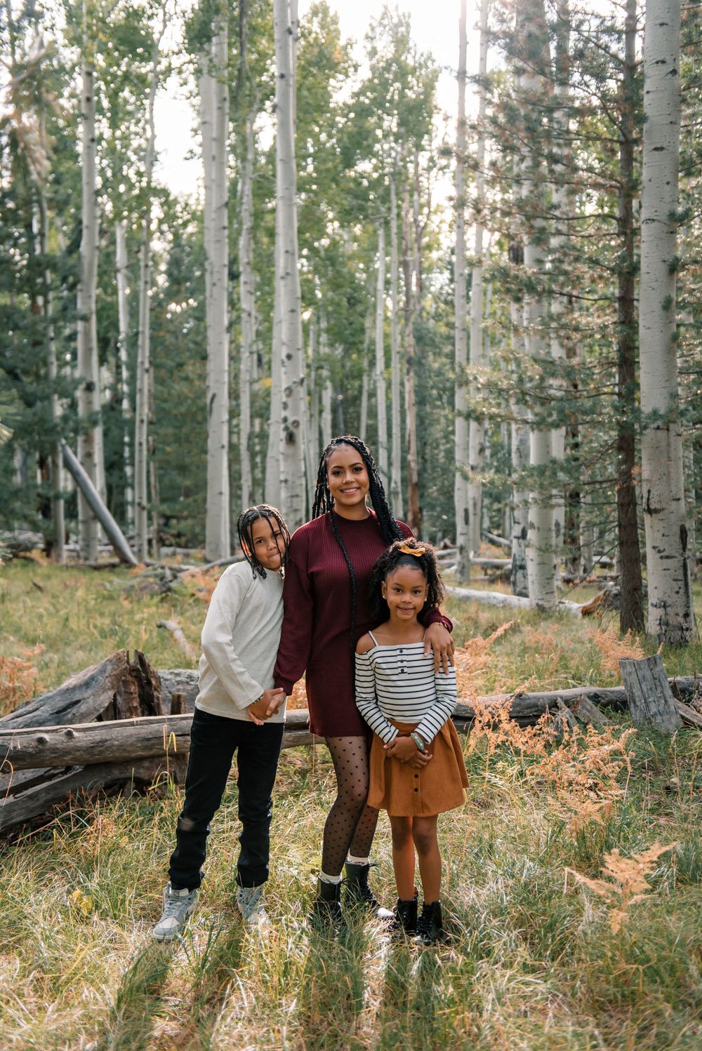 Family group photo in aspen forest wearing coordinated autumn outfits among fallen logs.