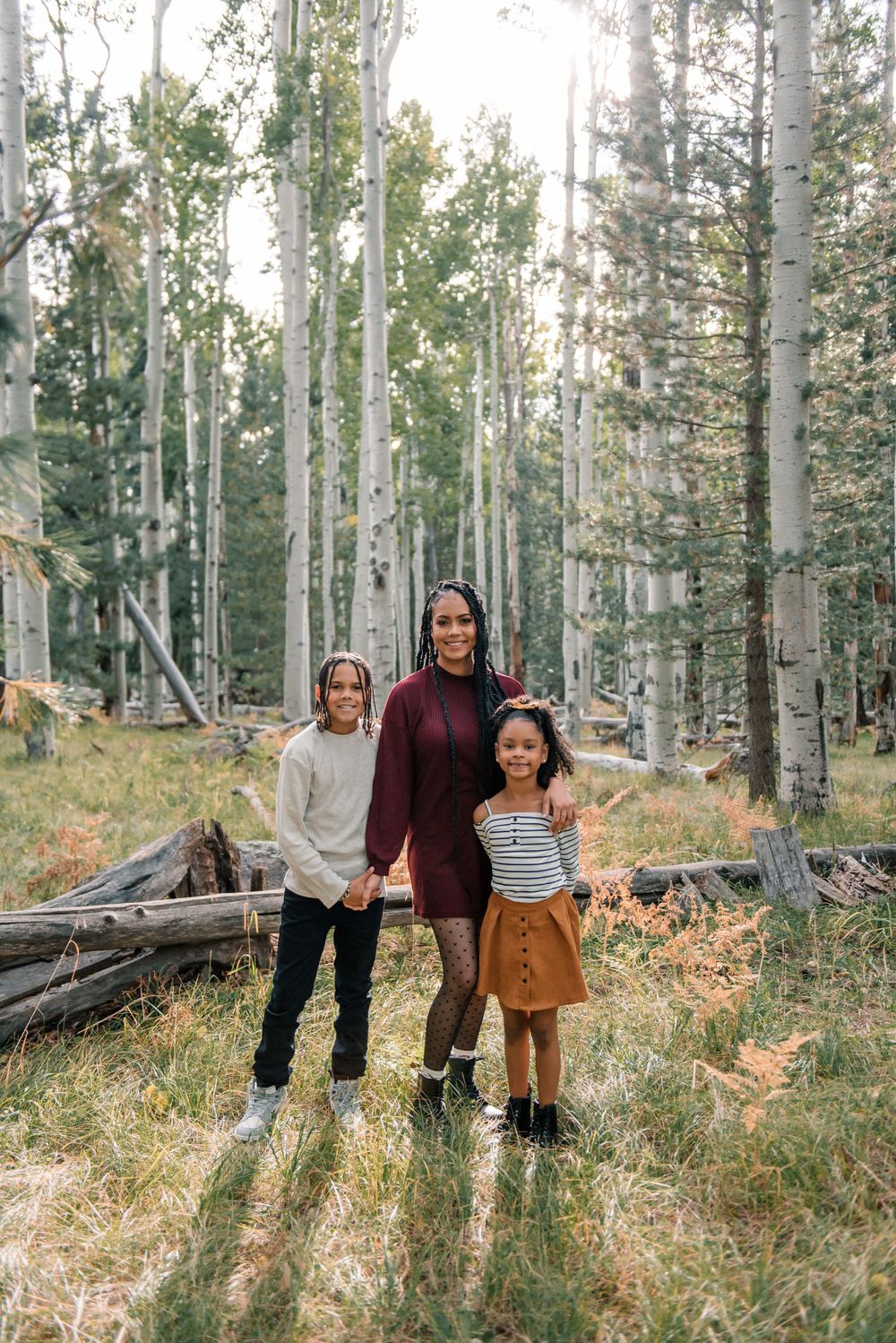 Family standing together in sunlit aspen forest wearing coordinated fall colors.