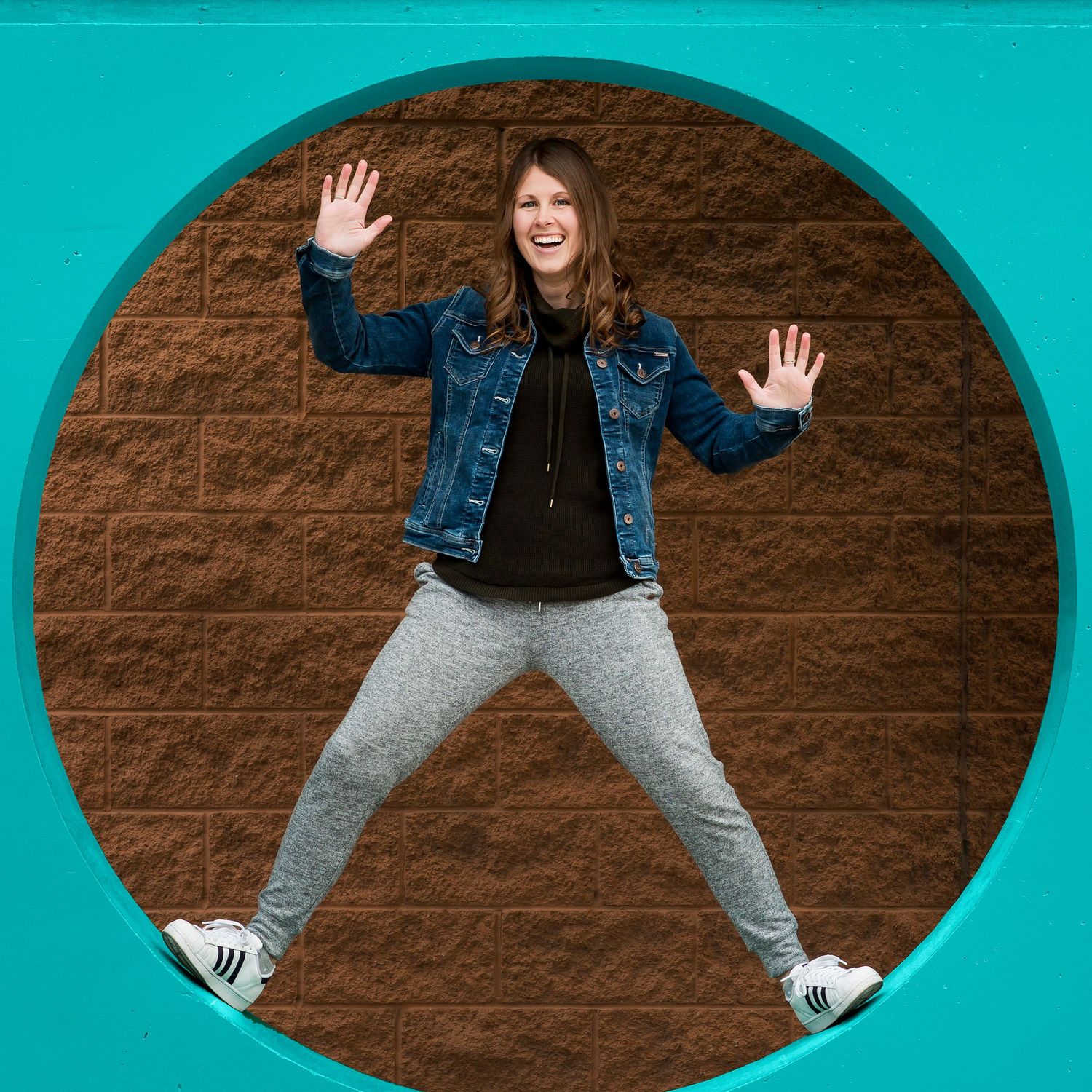Fun female Photographer smiling miming in Adidas tennis shoes, Roots pants and a blue jean jacket.