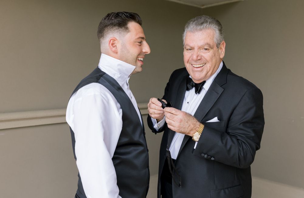 Two men in formal attire share a lighthearted moment in a hallway.
