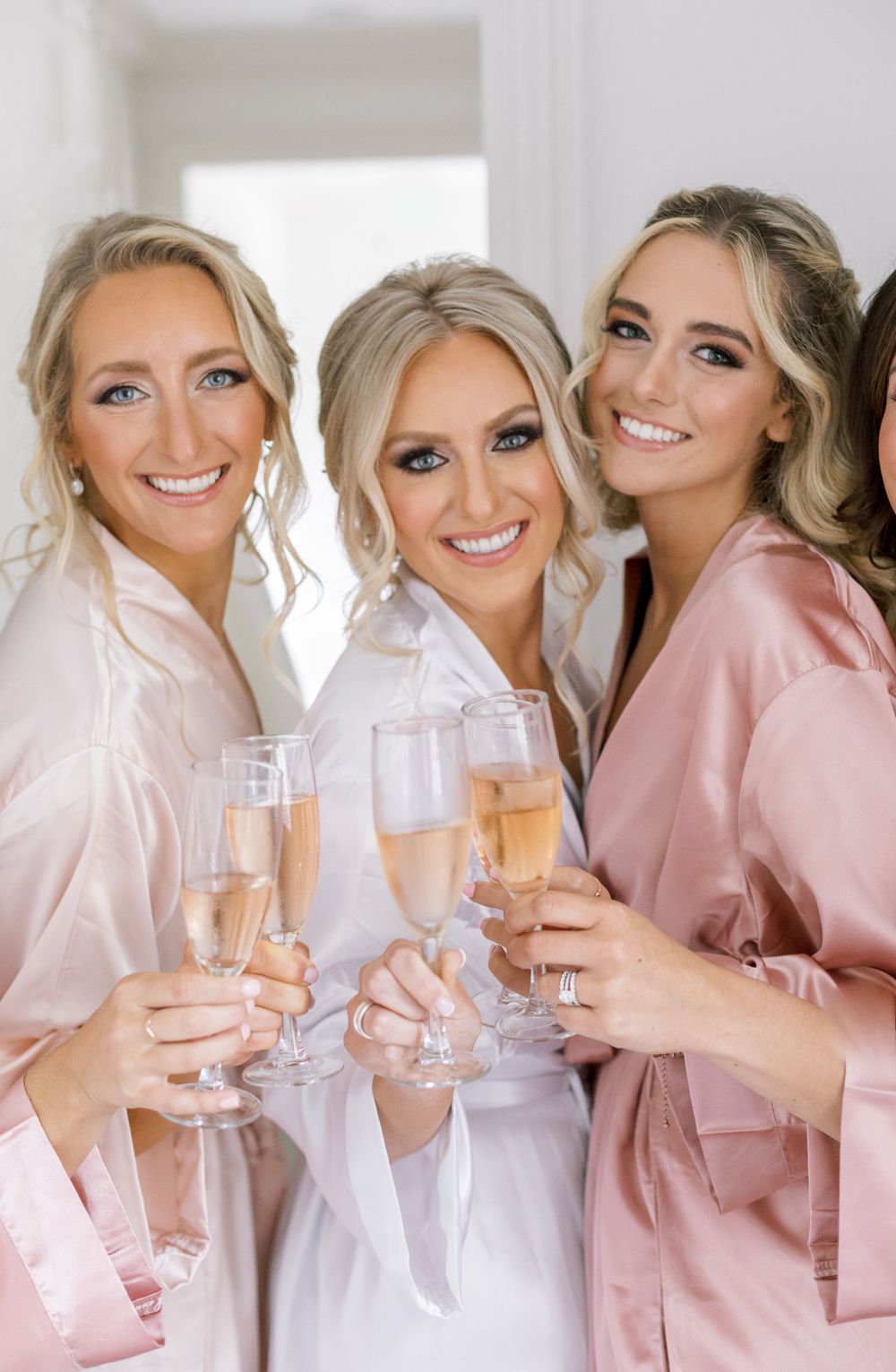 Friends in silk robes toasting with champagne during wedding preparation.