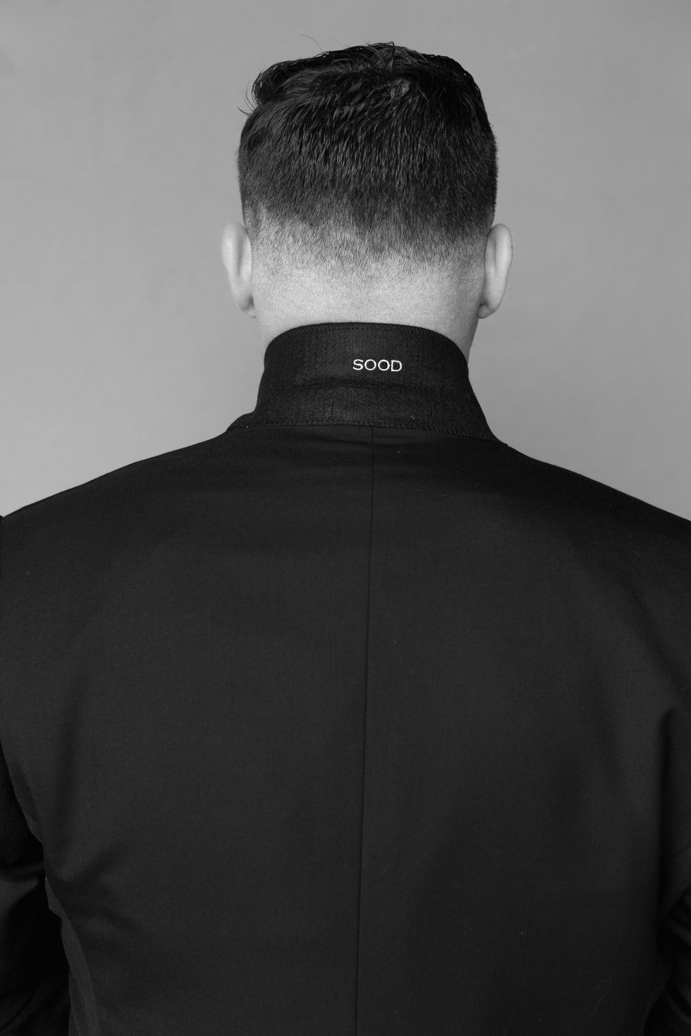 Back view of man wearing formal black suit with 'good' text on collar.