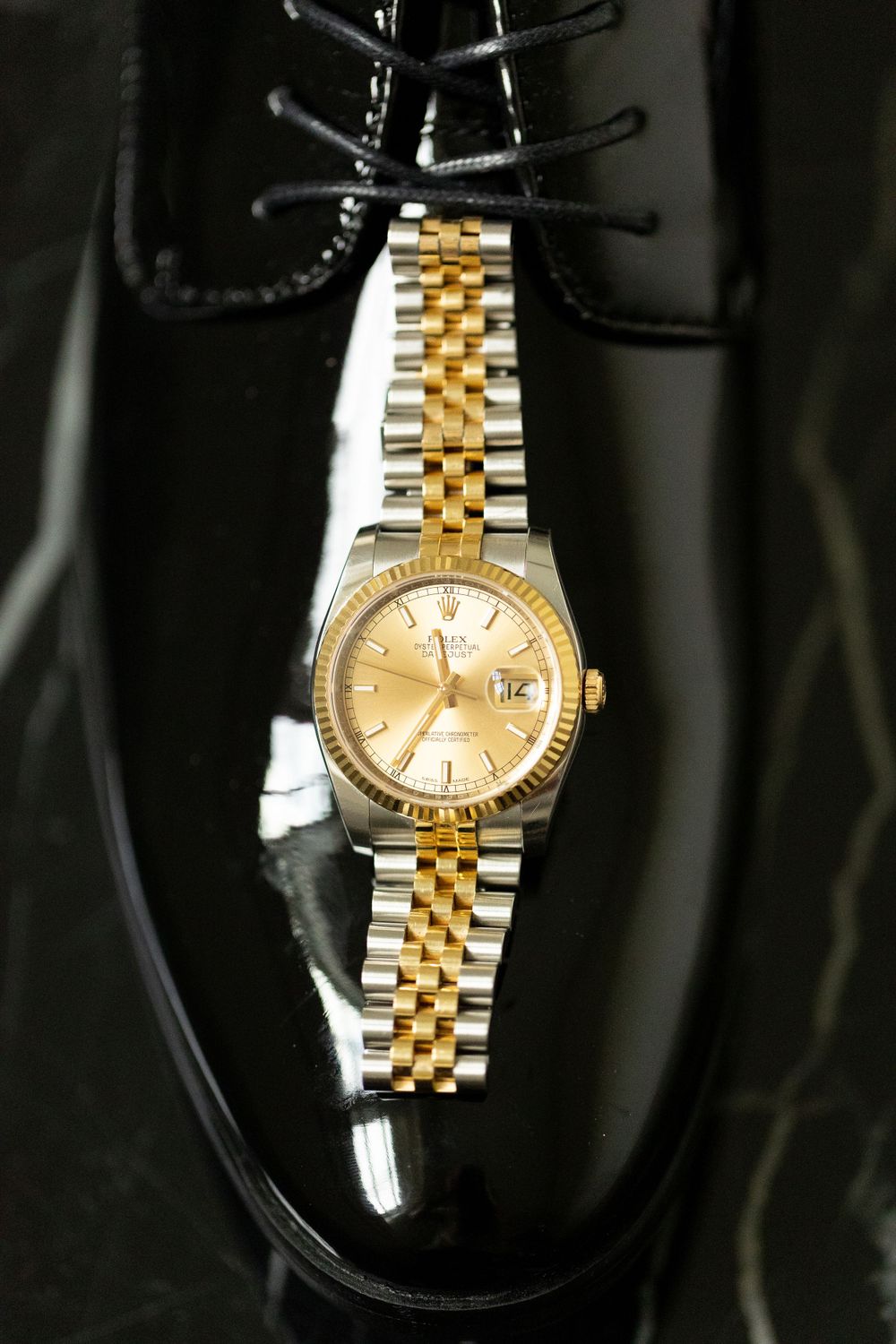 Two-tone gold and silver Rolex watch displayed on shiny black dress shoe.