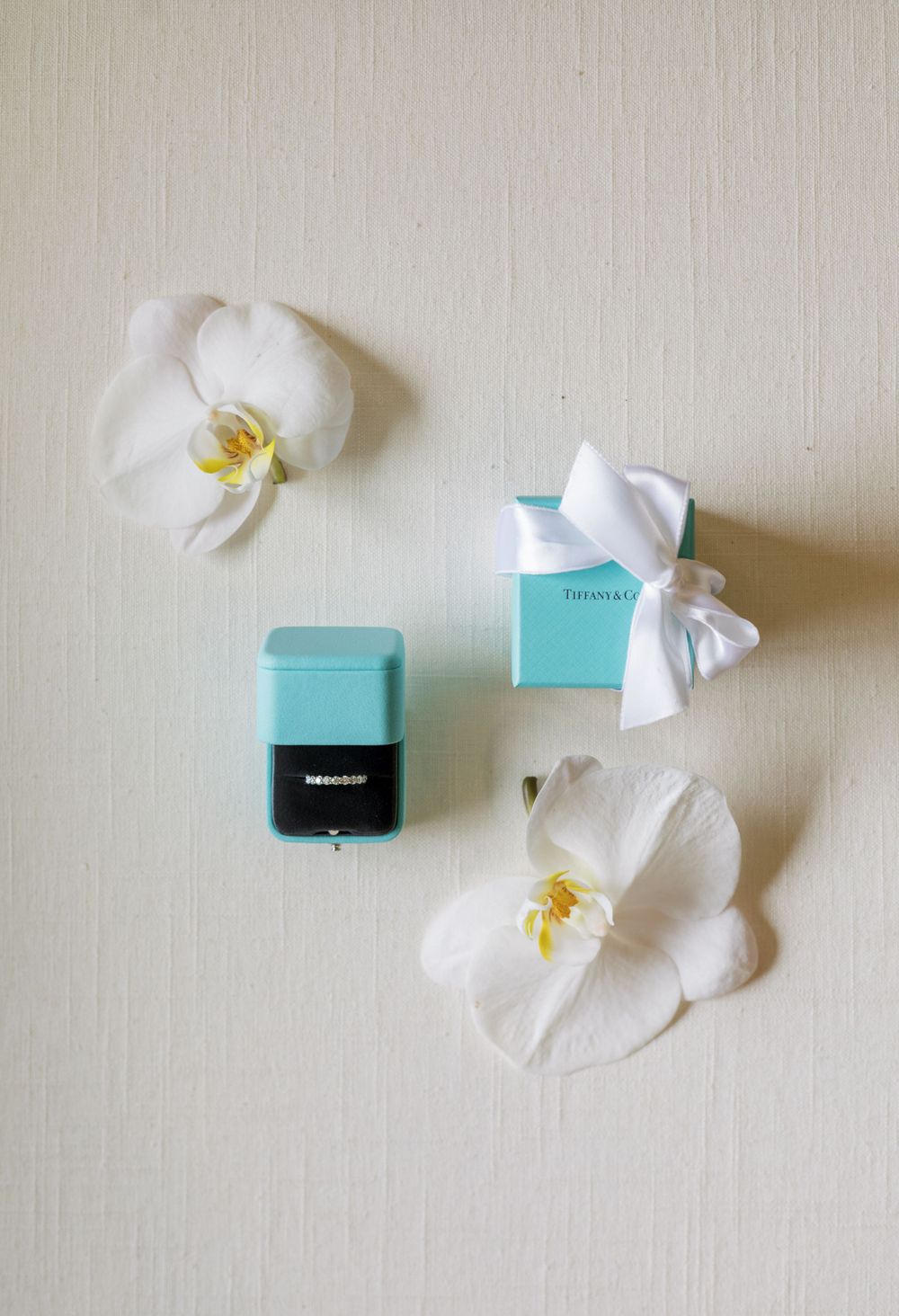 Tiffany blue ring box with white orchids and ribbon on light background.