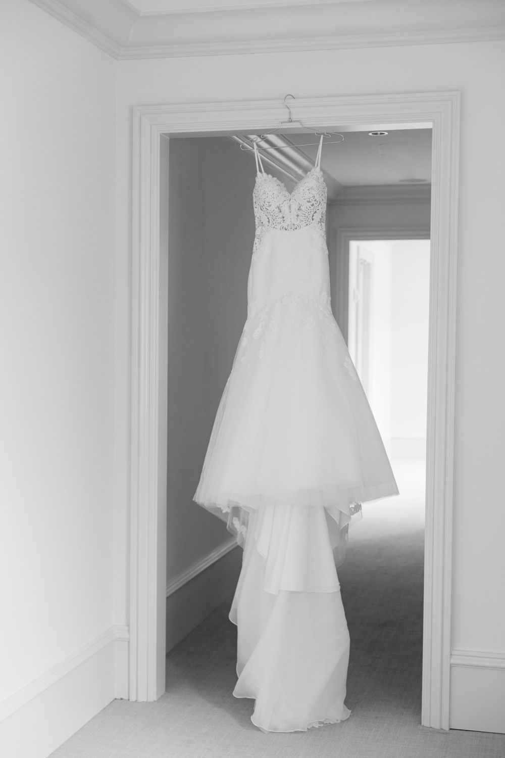 White lace wedding gown hanging in doorframe showing intricate detail and full tulle skirt.