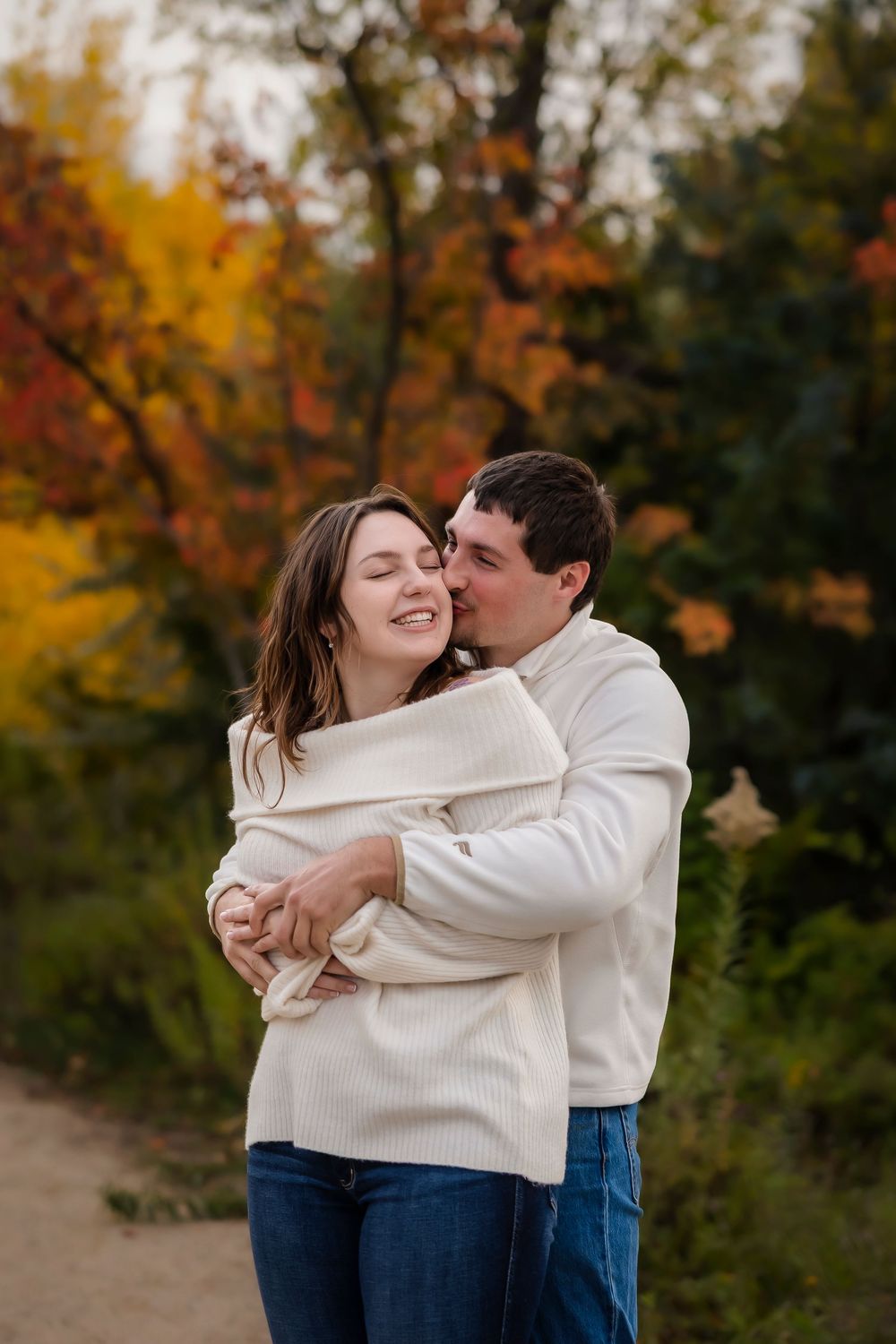 man kissing woman's cheek in front of autumn tree
