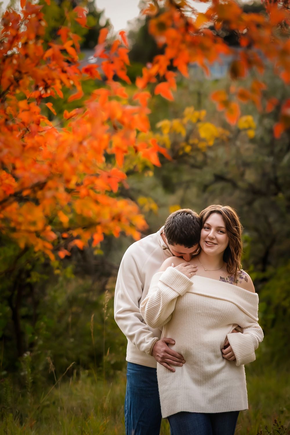 man kissing woman's shoulder in front of autumn tree