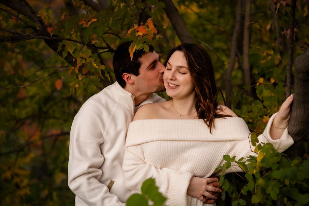 man kissing woman's cheek iunder autumn tree