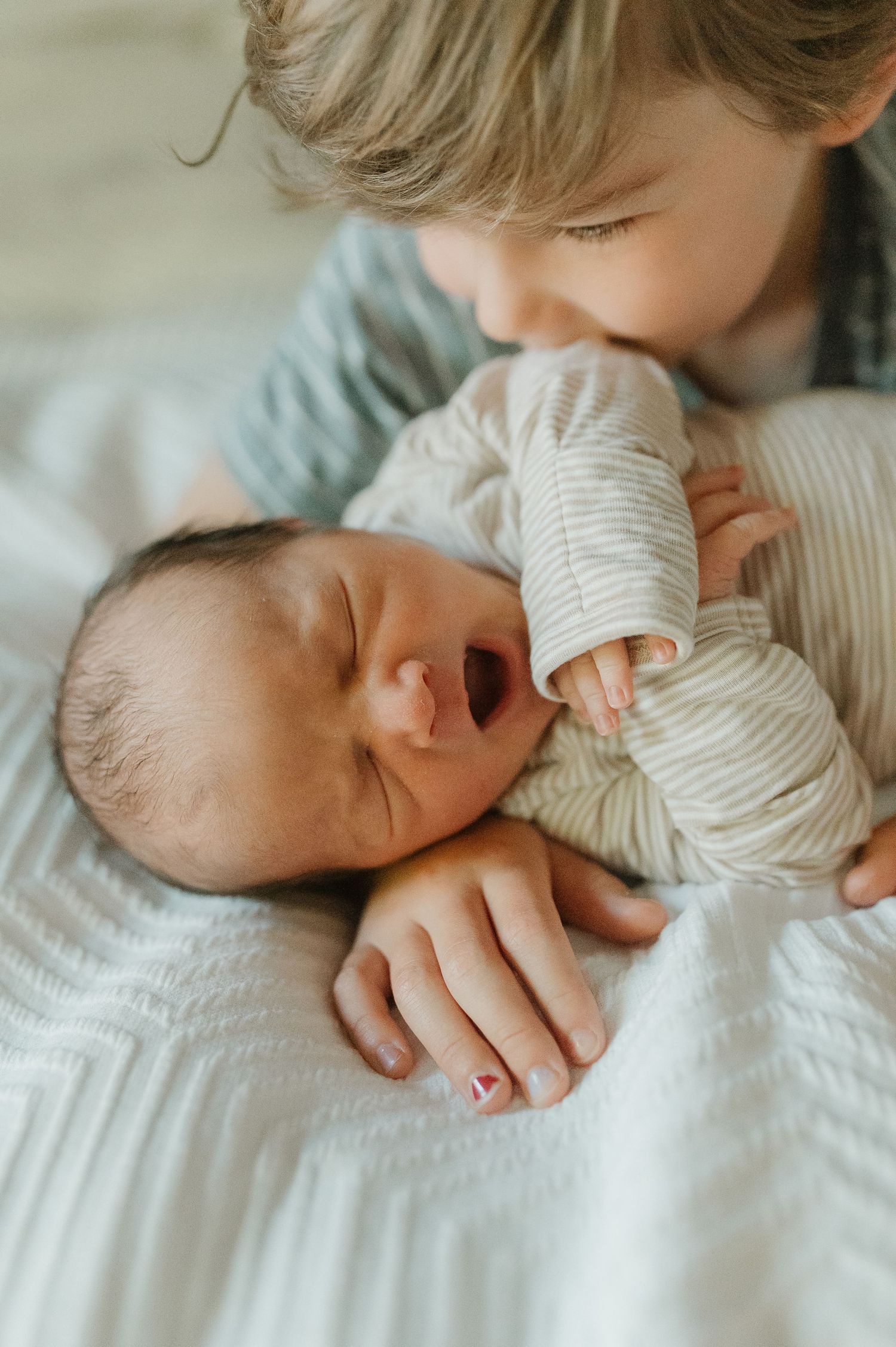A tender moment between two siblings as an older child gently kisses a sleeping newborn.