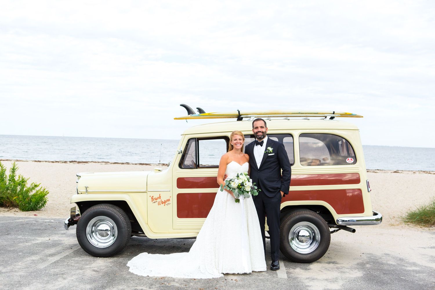 Vintage woody station wagon with surfboard parked at the beach on a cloudy day.