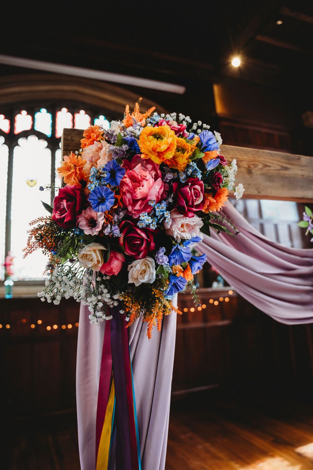 Colorful floral arrangements with pink draping decorate a wedding venue.