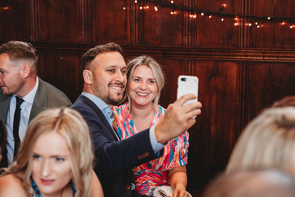 Wedding guests enjoying festivities in a wood-paneled hall decorated with string lights.