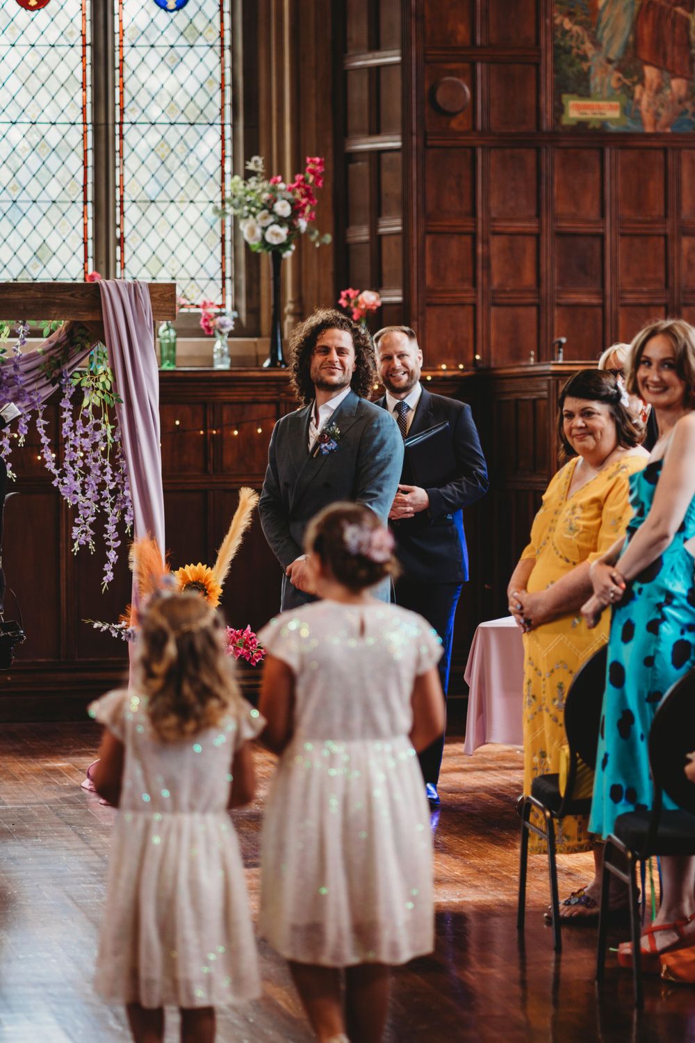 Wedding celebration with guests seated in historic venue decorated with flowers and string lights.