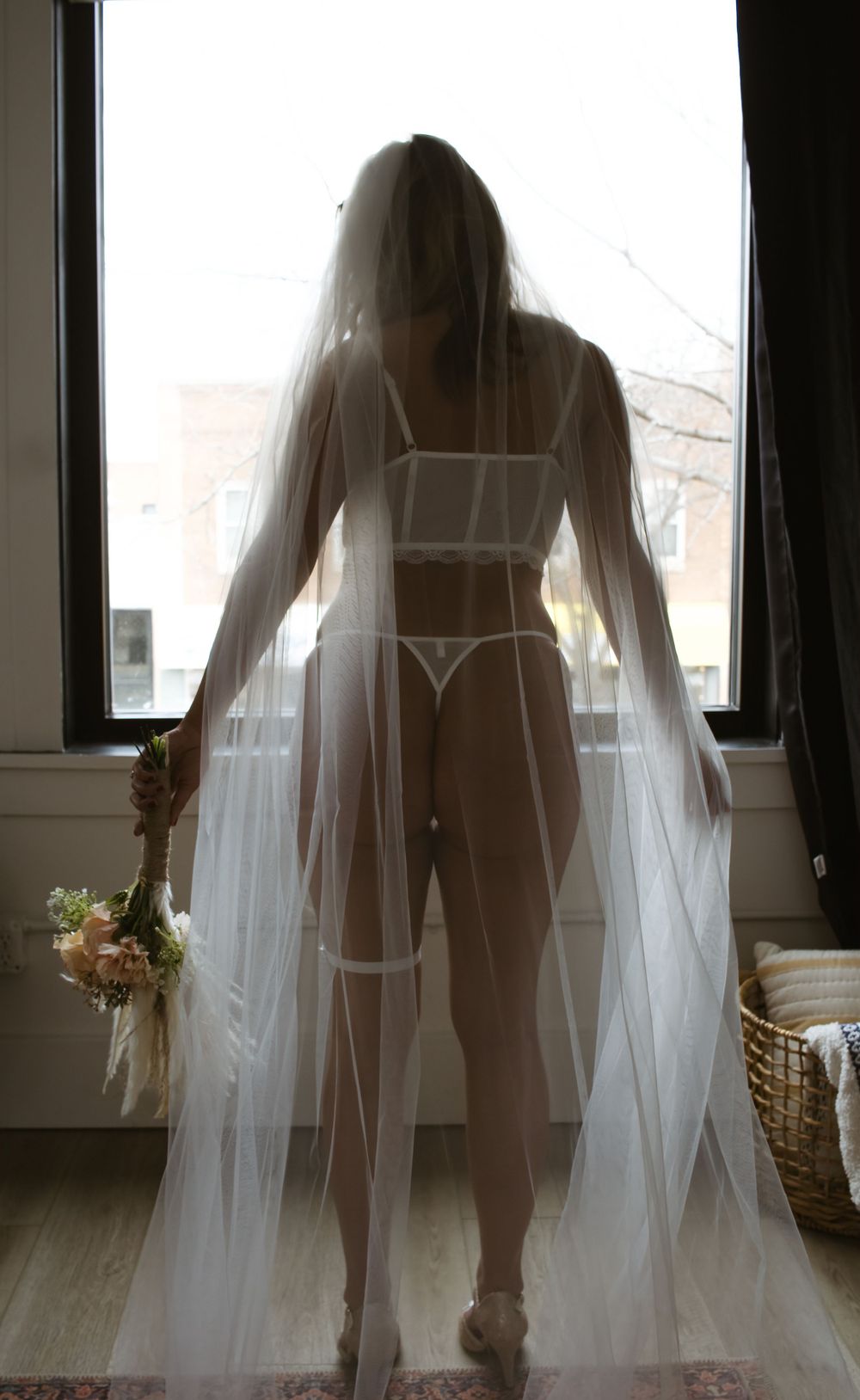 Silhouette of a figure in lingerie and veil standing backlit by sunlight through windows.