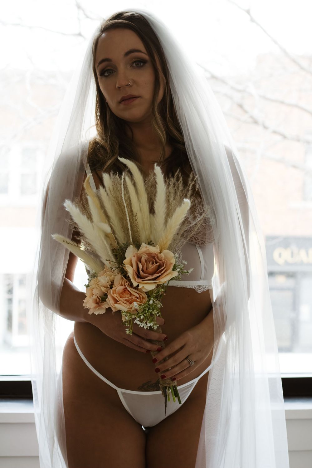 Bridal boudoir portrait with dried flower bouquet by window.