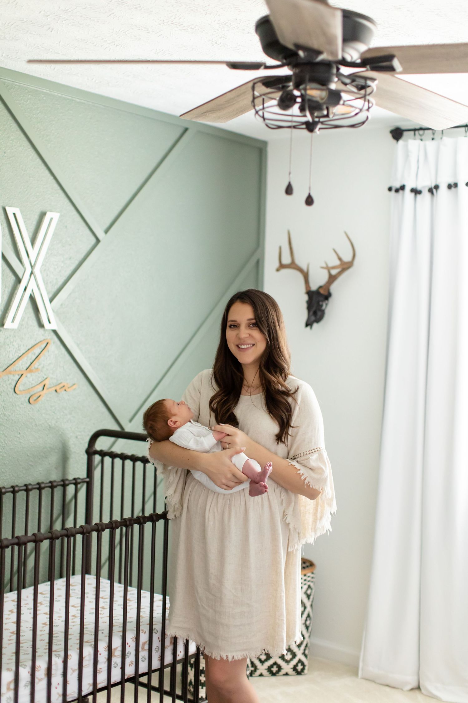 Modern nursery with geometric wall design and parent holding newborn by crib.