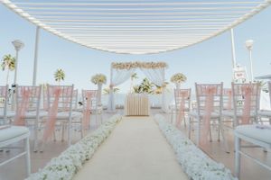 Outdoor wedding ceremony setup with white canopy and pink chairs along a flower-lined aisle.