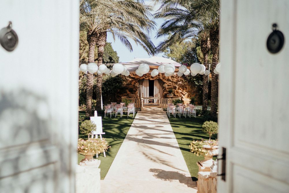 Palm-lined pathway leading to a wedding arch through elegant white doors.
