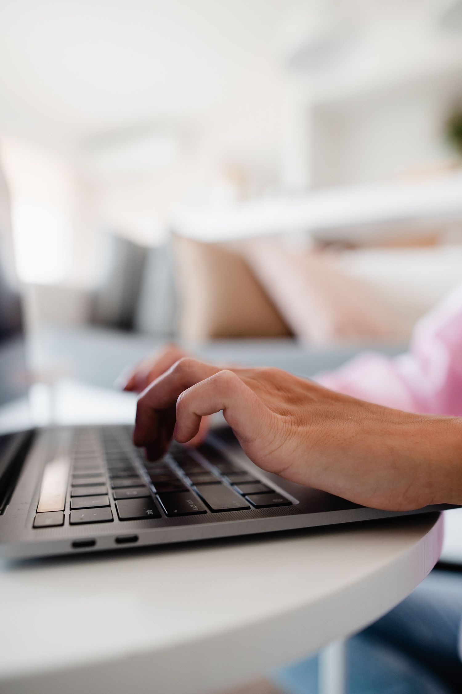 Closeup of hands typing on a modern laptop keyboard in a bright room.