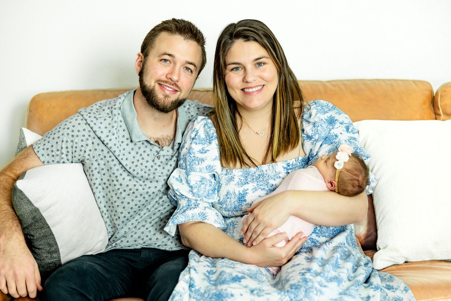 Parents sit on the couch with their new baby girl and smile during lifestyle newborn photos in Colorado Springs.