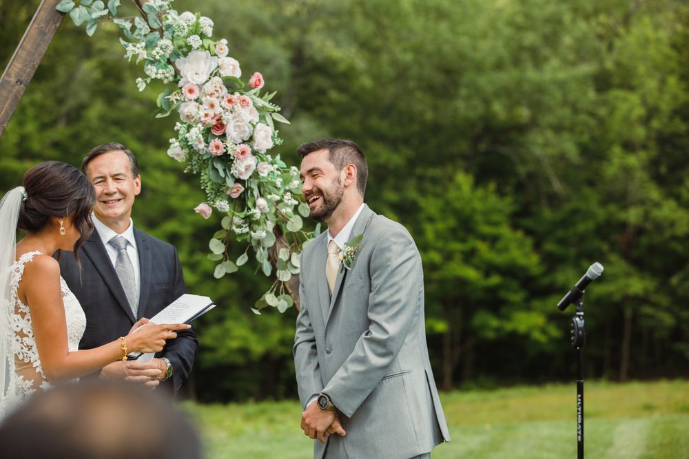 Outdoor wedding ceremony setup with white floral arch and mountain backdrop.