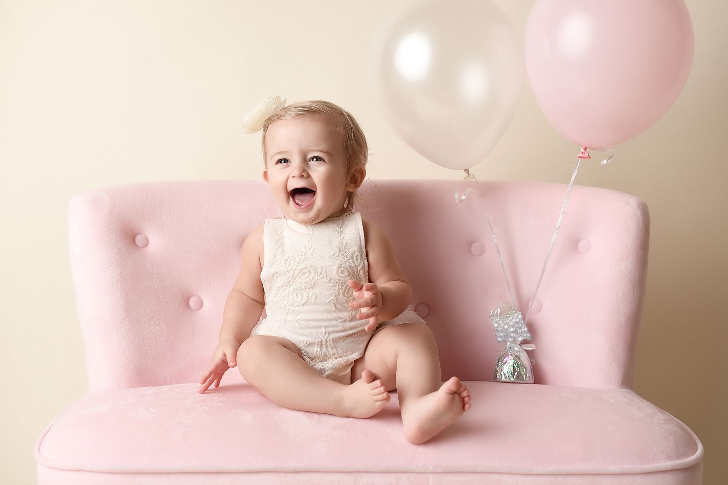 One year old sitting on a pink couch with balloons