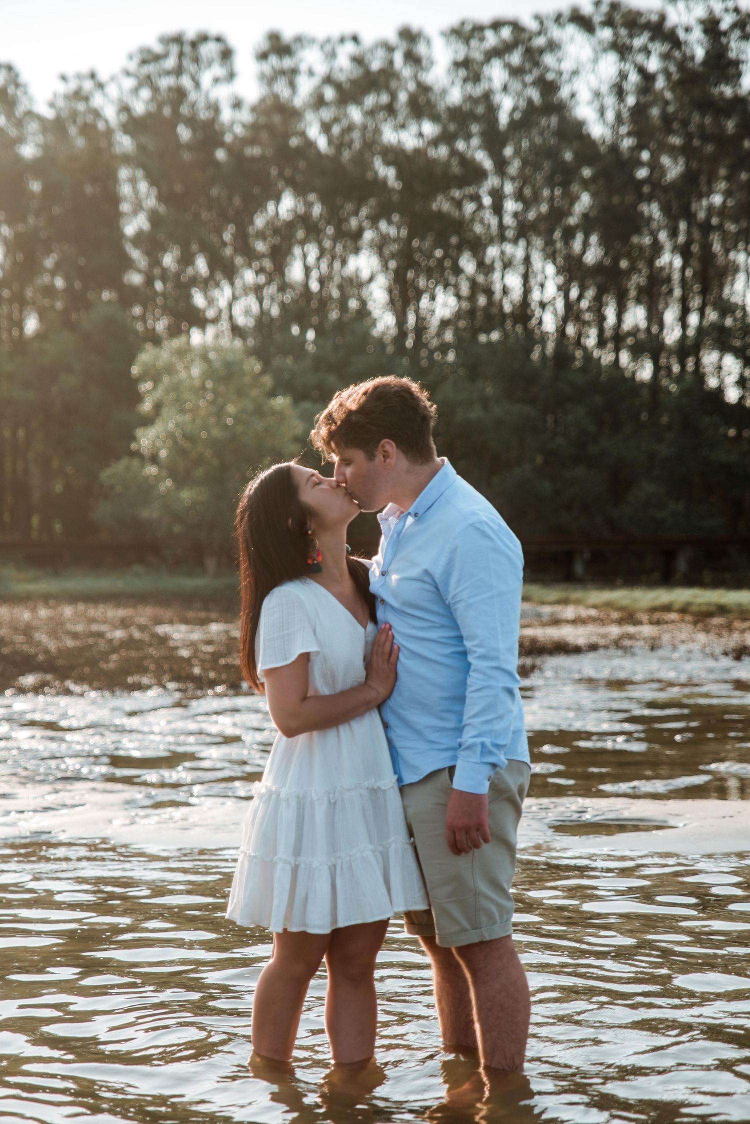 A romantic couple shares a tender moment while standing in shallow water at sunset.