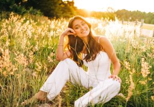 Person relaxing in white outfit among tall grass during golden sunset.