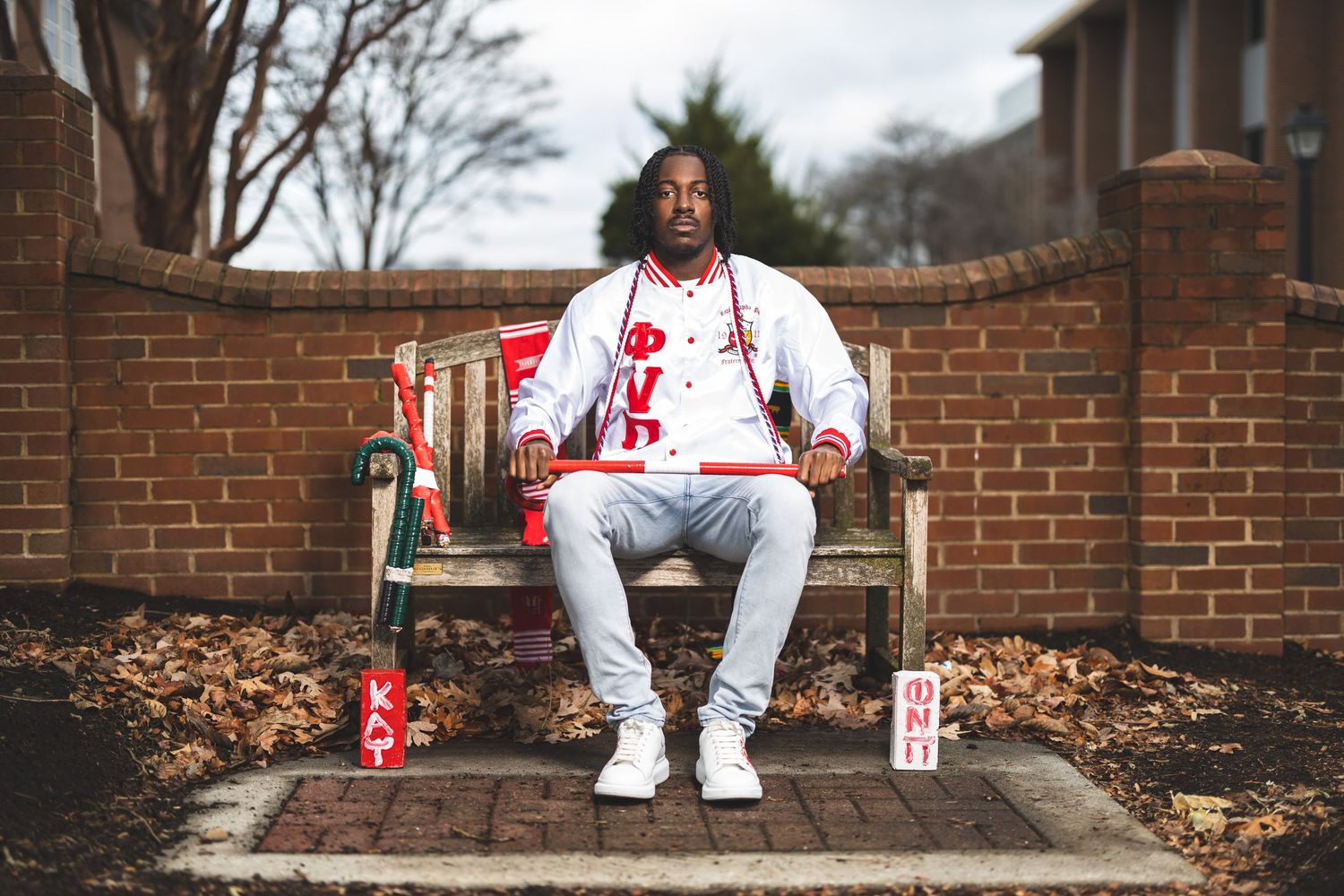 Graduate in white outfit sitting on brick wall bench with decorative red cans.