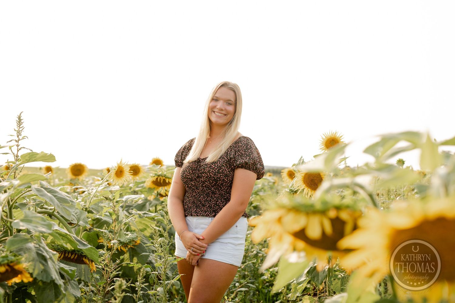 A summer portrait taken in a vibrant sunflower field with warm evening light.