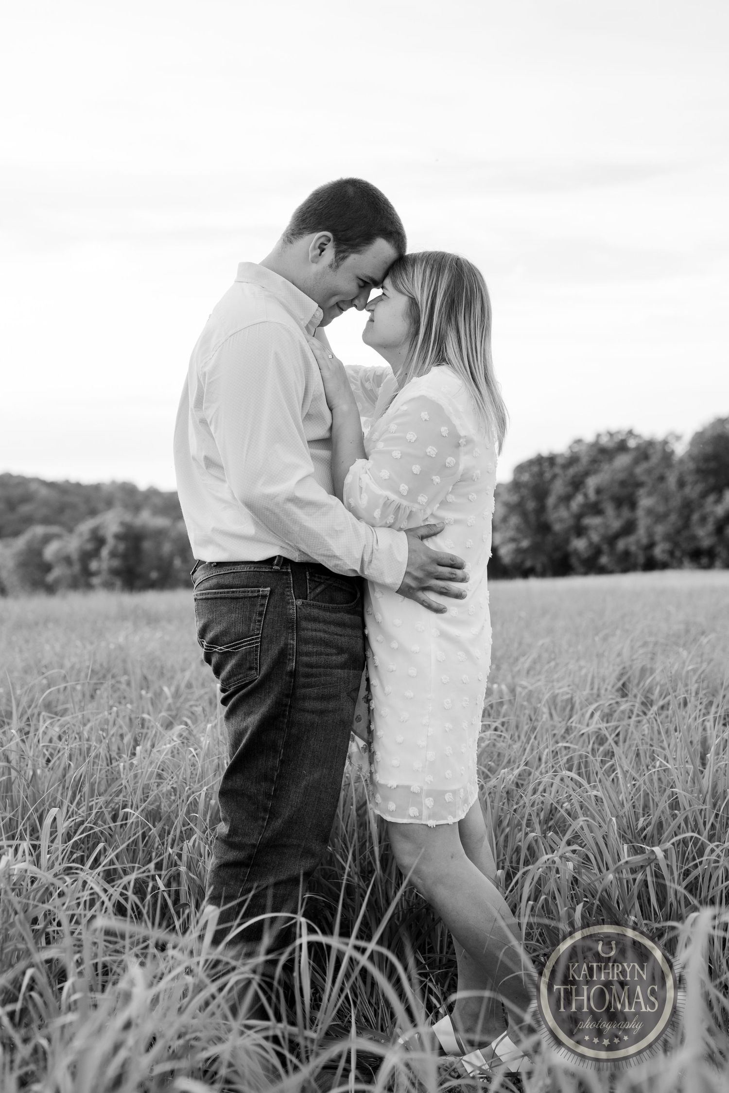 A couple embraces in a field of tall grass captured in black and white.